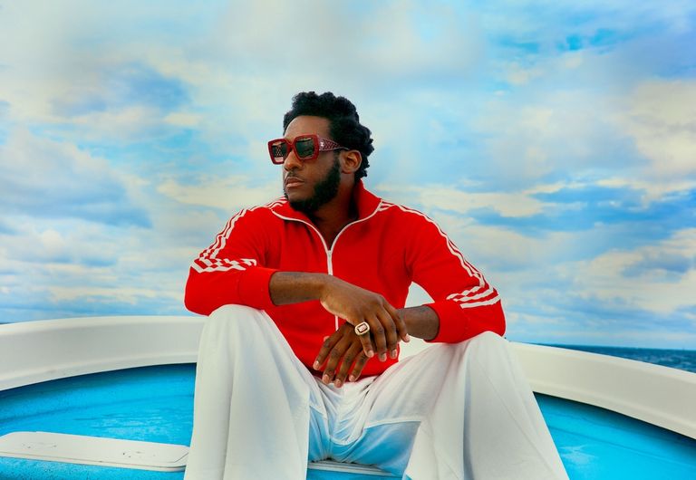 Soul musician Leon Bridges wearing a red track jacket and sunglasses aboard a boat, photographed outdoors against a blue sky by Joshua Kissi.